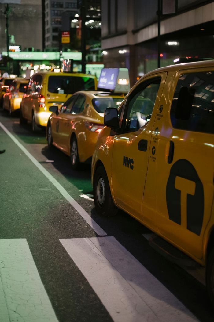contact-img Row of modern various yellow taxi vehicles parked on city street near buildings in New York at night