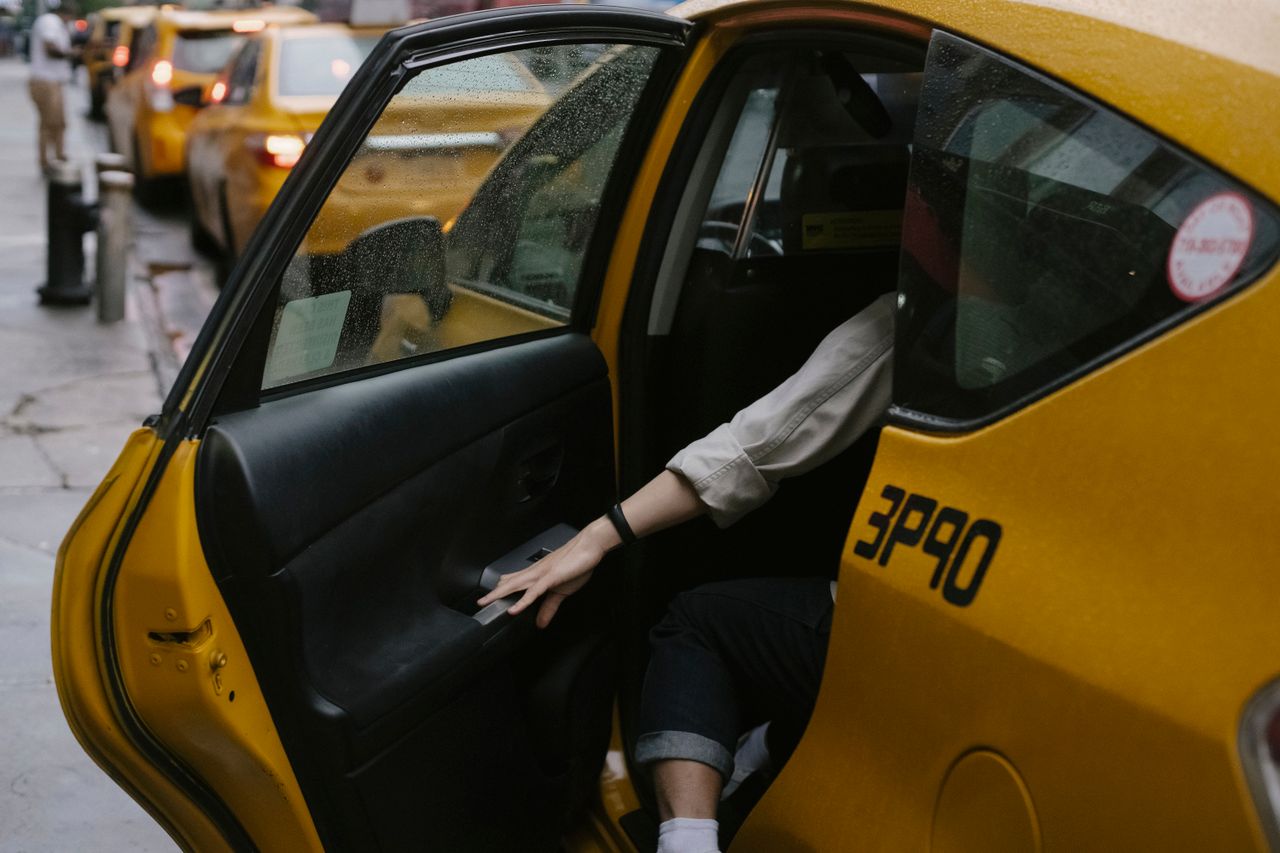 Anonymous passenger closing door of cab parked on roadside with blurred cars on background in rush hour on street in city